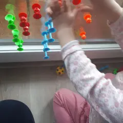 Roczne dziecko bawi się kolorowymi przyssawkami na oknie, tworząc kreatywne zabawy.