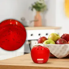 Czerwona pułapka na muszki owocówki w kuchni, obok koszyka z owocami. W zbliżeniu widać, jak owady wpadają do środka.