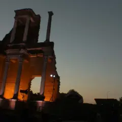 Il teatro romano di Volterra illuminato di sera, con le sue antiche colonne che emergono dall'ombra.