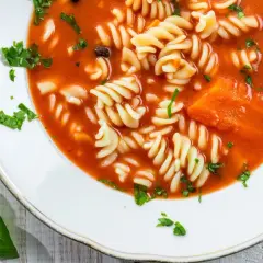 Zupa pomidorowa z makaronem fusilli i kawałkami marchewki. Aby jak zmniejszyć kwasowość zupy, dodaj szczyptę sody.