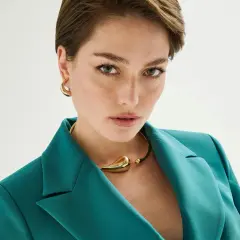 Mujer con un elegante corte pixie, viste un blazer verde azulado y un collar dorado.