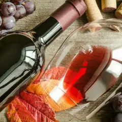 Uva Sangiovese, vitigno del Brunello di Montalcino, accompagna una bottiglia e un calice di vino rosso, su un tavolo di legno rustico.