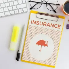 Ubezpieczenie zdrowotne bez pracy: dokument z napisem "INSURANCE" i ikoną parasola. Obok klawiatura, okulary, kawa.