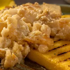 Un saporito baccalà alla vicentina, cremoso e profumato, servito su fette di polenta grigliata.