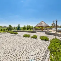 Piękny ogród z krętymi ścieżkami wyłożonymi kostką granitową, altaną krytą strzechą i basenem pod kopułą.
