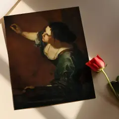Obraz przedstawia kobietę malującą obraz, co jest alegorią sztuki i kreatywności. Obok leży czerwona róża.