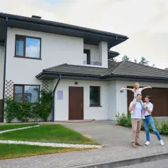 Szczęśliwa rodzina przed nowoczesnym domem. Czy to odzwierciedla realny koszt budowy domu?