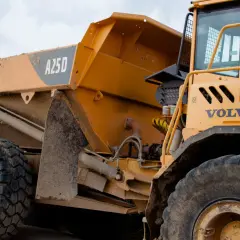 Żółte, masywne **Volvo wozidlo** budowlane z błotem na karoserii i oponach. Widoczna kabina i część skrzyni ładunkowej z oznaczeniem A25D.