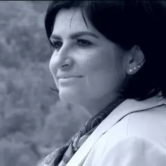 Portret Agnieszki Kołacz Leszczyńskiej w białej marynarce, z delikatnym uśmiechem i ozdobnymi kolczykami.