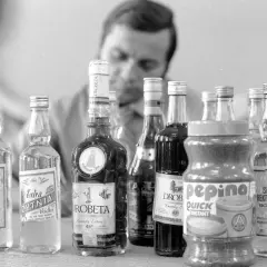 Mężczyzna bada butelki z alkoholem, w tym wódkę i brandy. Proces kupażowania może prowadzić do mętnienia wódki po dodaniu wody.