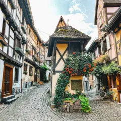 Kopfsteinpflastergasse im Elsass mit Fachwerkhäusern, Blumen und einem Fahrrad. Ein perfekter Ort für Geheimtipps im Elsass.