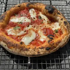 En perfekt napolitansk pizza med bubblig, bränd kant, tomatsås och smält mozzarella på ett galler.