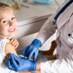 Niña sonriente recibe vacuna contra la gripe. Es recomendable vacunar a los niños de la gripe para proteger su salud.