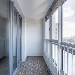 Szare okna i drzwi balkonowe, biała balustrada i widok na miasto. Idealne miejsce, by zastanowić się, czym osłonić balkon.