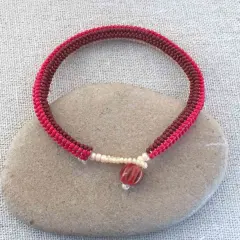 Braccialetto fatto a mano con nodi per braccialetti elastici, perline rosse e marroni, e una perlina centrale striata.