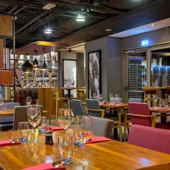 Elegancka restauracja w hotelu Mercure Wrocław Centrum. Drewniane stoły, czerwone i szare krzesła, półki z winami.