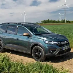 Dacia Jogger verde su sterrato, con pale eoliche sullo sfondo. Un'auto perfetta per un viaggio in autostrada con **GPL**.