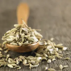 Drewniana łyżka pełna nasion kopru włoskiego, zwanego też kminkiem. Obok rozsypane nasiona, które dodadzą aromatu potrawom.