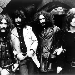 Czterech muzyków Black Sabbath, w tym wokalista, pozuje do zdjęcia w rockowych strojach.