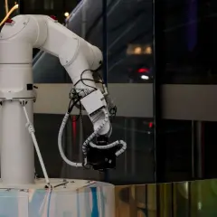 Białe ramię robota z kamerą, symbol postępu w dziedzinie generatywnej sztucznej inteligencji, gotowe do uchwycenia przyszłości.