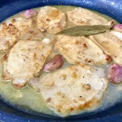 Filetes de lomo al ajillo dorándose en una sartén con ajo y laurel.