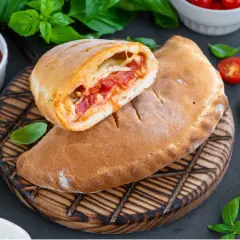 Złocisty calzone, przekrojony na pół, odsłaniający gorące nadzienie z pomidorów i sera. Obok sos pomidorowy i świeża bazylia.