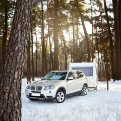 Biały SUV z przyczepą kempingową w zimowym lesie. Idealne warunki do podróży z prawem jazdy B+E.