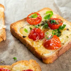 Tosty z serem, pomidorkami koktajlowymi i szczypiorkiem na papierze do pieczenia.