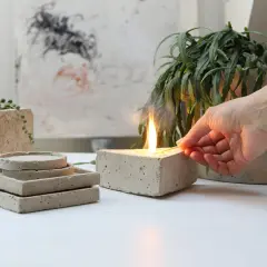 Accensione di una candela in un blocco di cemento, che ricorda come viene fatto il cemento. Piante e sottobicchieri in cemento completano la scena.