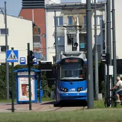 Niebieski tramwaj linii 20 na przystanku, obok rowerzysta i budynki.