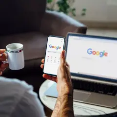 Mężczyzna z kubkiem kawy przegląda instrukcję, jak wylogować się z konta Google, na telefonie i laptopie.