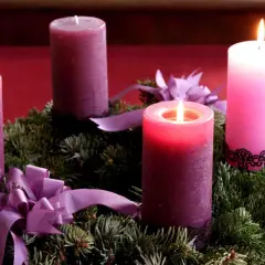 Drei von vier 3. Advent Kerzen brennen auf einem Tannenkranz mit lila Schleifen.