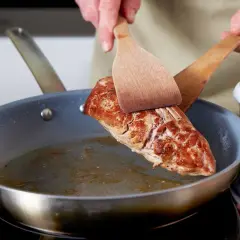 Ein saftiges Schweinefilet braten in der Pfanne. Mit zwei Holzspateln wird das Fleisch gewendet, um es von allen Seiten perfekt zu garen.