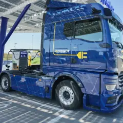 Niebieska ciężarówka elektryczna MAN eTGX z logo "epower" ładuje się pod panelem słonecznym. To przyszłość transportu, zgodna z normą euro 7.