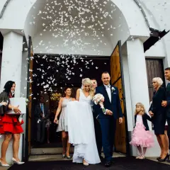 Młoda para wychodzi z kościoła, obsypana płatkami w kształcie motyli. To piękny motyw tradycji w weselu, symbolizujący szczęście i nowy początek.