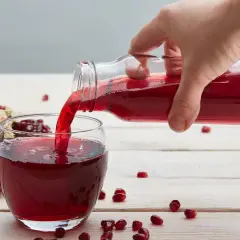Ręka nalewa sok z granatu do szklanki. Obok leży połówka owocu. Ile pić dziennie?