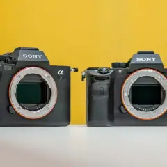 Dwa aparaty Sony Alpha, jeden z nich to sony a7 iiis, stoją obok siebie na białej powierzchni, na żółtym tle.