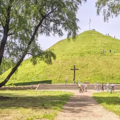 Zielony Kopiec Piłsudskiego z krzyżem i ludźmi spacerującymi po zboczu.