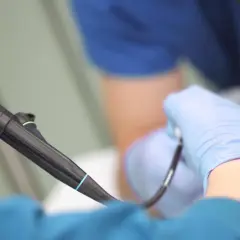 Ręce w niebieskich rękawiczkach trzymają endoskop. Przygotowanie do gastroskopii w toku.