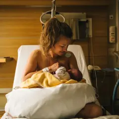 En mamma ammar sitt nyfödda barn på en sjukhussäng. En lugn stund efter förlossningen, kanske inför en efterkontroll på MVC.