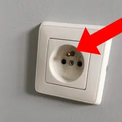 Czerwona strzałka wskazuje na gniazdko elektryczne, gdzie próbnik świeci na bolcu, sygnalizując obecność napięcia.