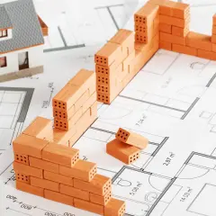 Model domu i mury z cegieł na planie architektonicznym symbolizują początek budowy domu.