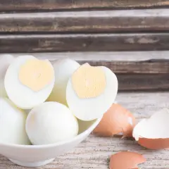 Un bol de blancs d'œufs durs, certains coupés en deux, prêts pour la conservation. Des coquilles d'œufs brisées à côté.