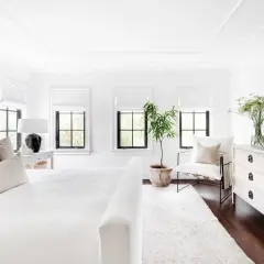 A serene, feminine black and white bedroom with a plush white bed, textured pillows, and a black lamp.