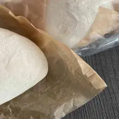 Frische Pizzaböden, bereit für das Pizzateig einfrieren. Einer liegt auf Backpapier, weitere sind in Folie verpackt.