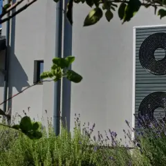 Nowoczesna pompa ciepła przy domu, otoczona lawendą. Czy pompa ciepła jest głośna? Ten model działa cicho, nie przeszkadzając w odpoczynku.