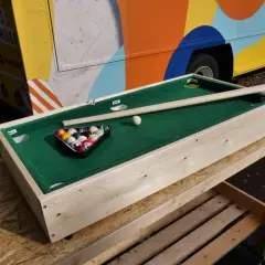 Ein kleiner Billardtisch, der zum Esstisch umgebaut werden kann, mit Kugeln und Queue.