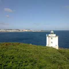 El faro de Mera se alza blanco sobre un promontorio verde, vigilando la costa y el mar azul.