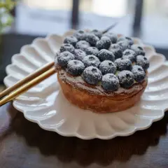 Tarte myrtille Savoie, une gourmandise aux myrtilles fraîches saupoudrée de sucre glace, servie sur une assiette blanche.