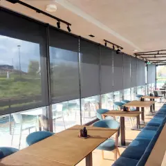 Nowoczesne wnętrze restauracji z widokiem na wodę, osłonięte eleganckimi roletami termicznymi na wymiar.